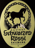 Oval yellow-green Gasthof Schwarzes Rössl Salzburg luggage label with black horse silhouette, decorative wreath and stylised buildings